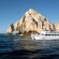 A catamaran filled with passengers cruising alongside the El Arco rock formation in Cabo San Lucas